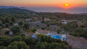 A residential area with houses, a swimming pool, and a view of the sea at sunset.