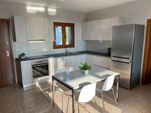 Une cuisine moderne dotée d’un îlot central, d’appareils électroménagers en acier inoxydable et d’une fenêtre avec des stores.