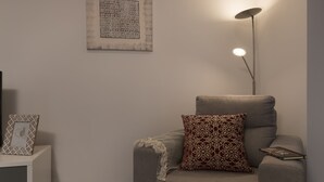 Un salon moderne avec un canapé gris, des coussins à motifs, une lampe sur pied et une œuvre d’art encadrée accrochée au mur.