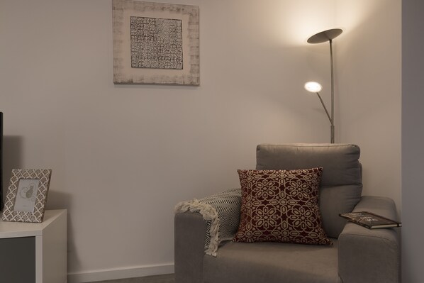 A modern living room with a grey sofa, patterned cushions, a floor lamp, and a framed artwork on the wall.