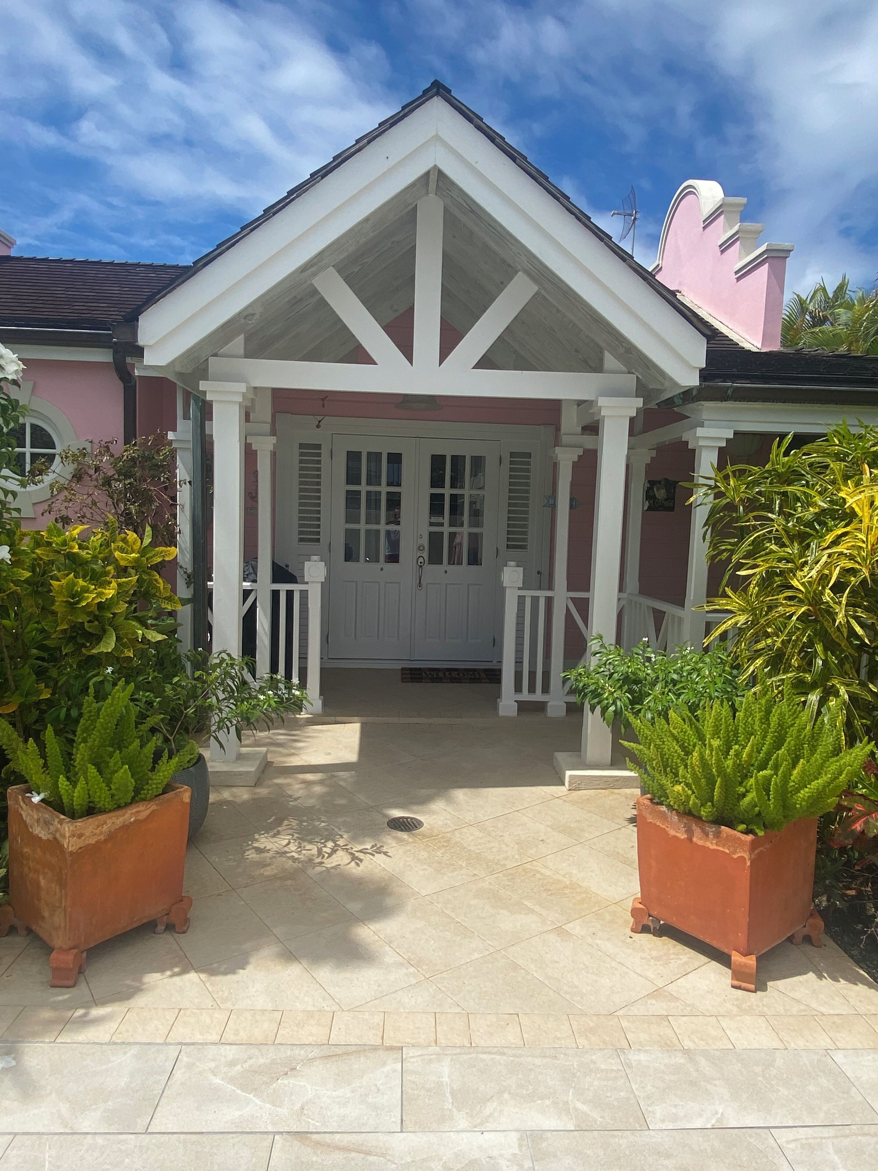 A house with a white porch, a pink wall, and a tiled entrance.