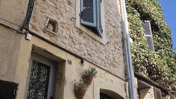 Ein Gebäude mit strukturierter Fassade, einer Tür mit einem Metallgitter und Topfpflanzen im Erdgeschoss.