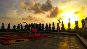 A playground with swings and a slide, surrounded by trees and a sunset in the background. - Comfy Home at Sutera Avenue (Kota Kinabalu)