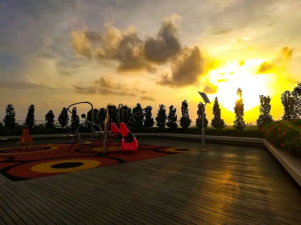 A playground with swings and a slide, surrounded by trees and a sunset in the background. - Comfy Home at Sutera Avenue (Kota Kinabalu)