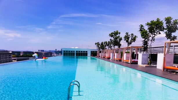 A rectangular swimming pool with clear blue water, surrounded by a wooden deck and a row of lounge chairs. - Comfy Home at Sutera Avenue (Kota Kinabalu)