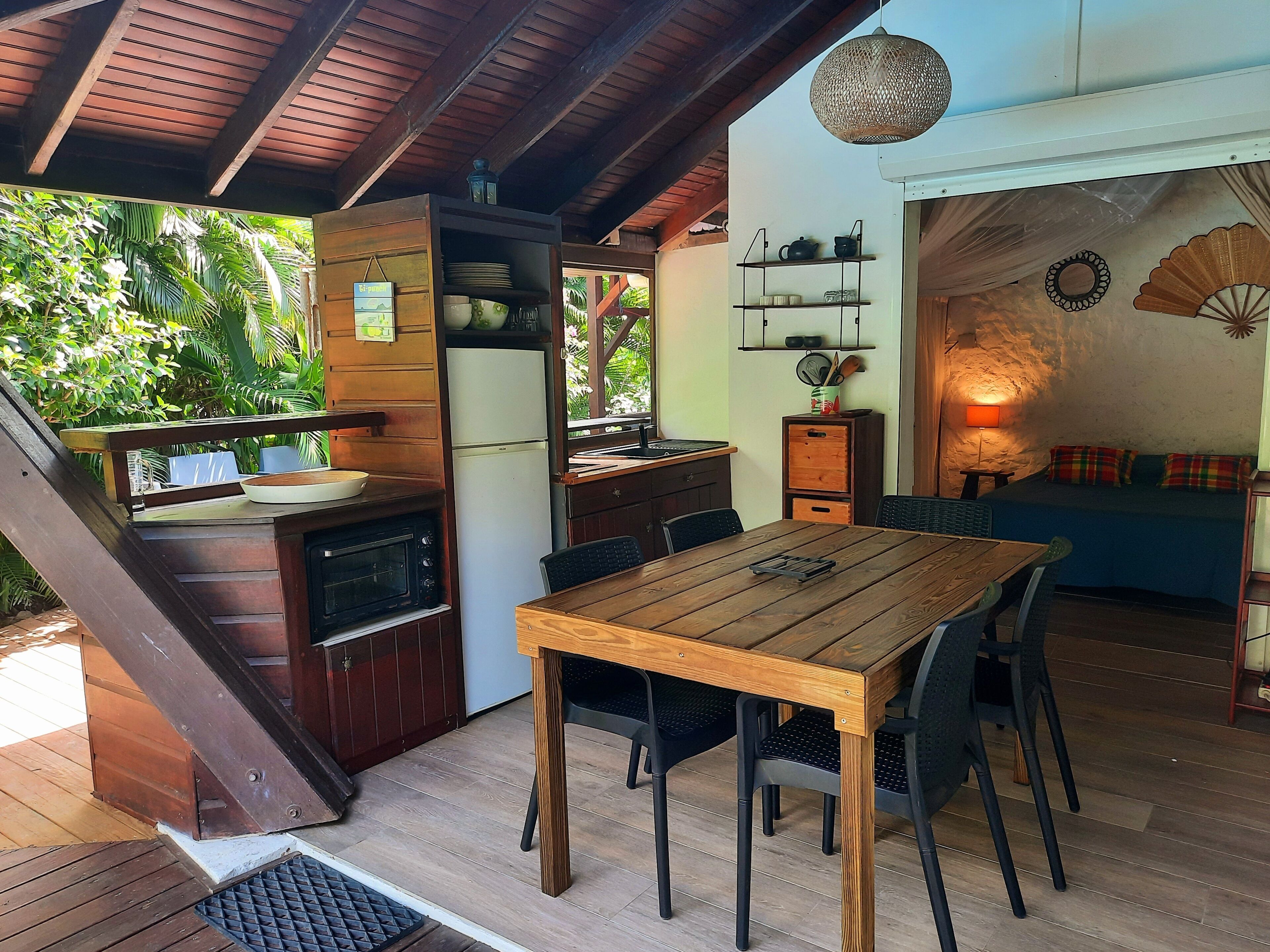 A wooden dining table with chairs, a kitchen area with a refrigerator and stove, and a cozy seating area with cushions.