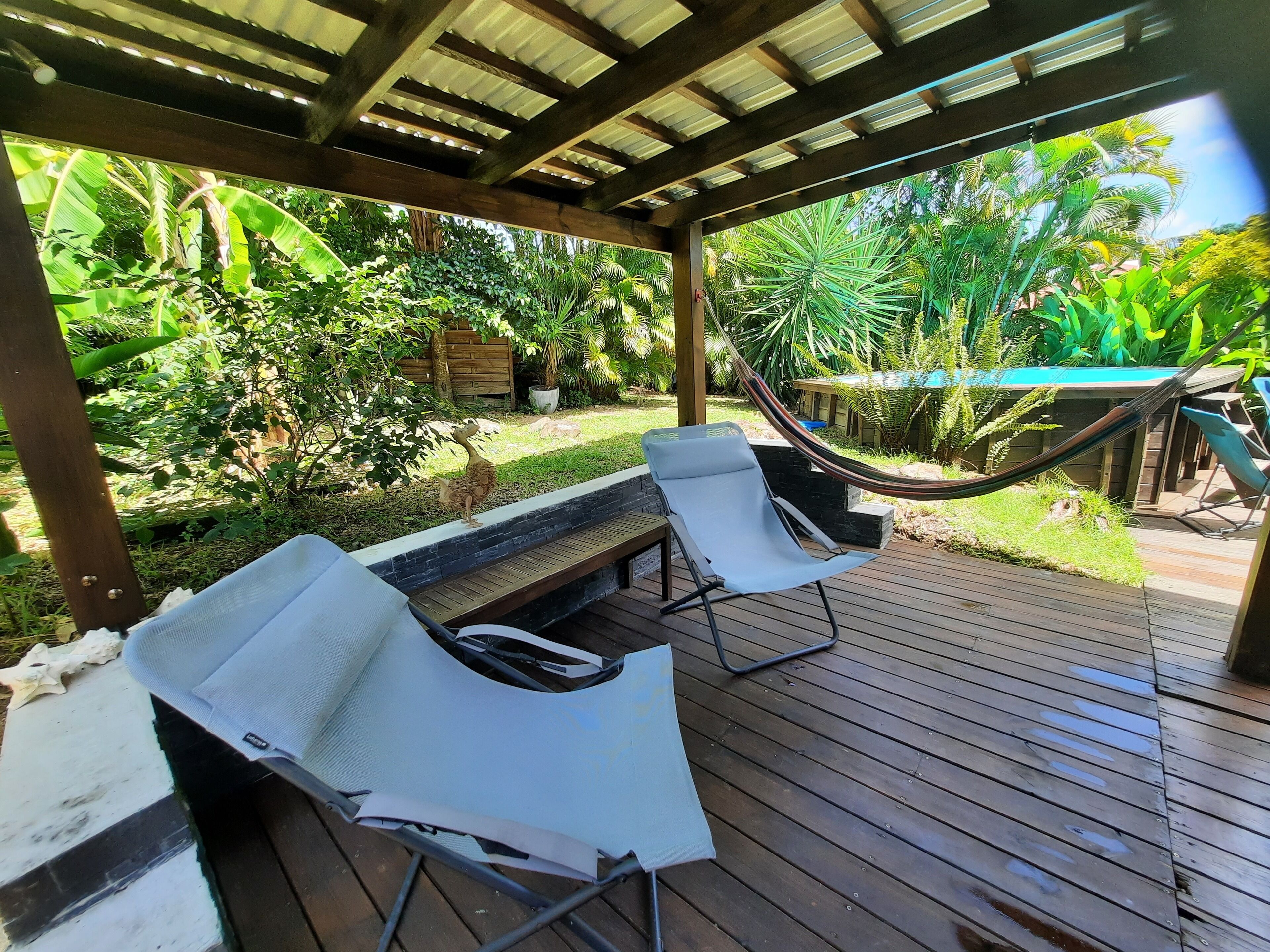 Un espacio al aire libre techado con terraza de madera, dos sillones blancos y una hamaca.