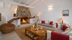 Un salon chaleureux avec une cheminée en pierre, des meubles blancs et une table basse en bois sur laquelle sont posés des livres et des en-cas.