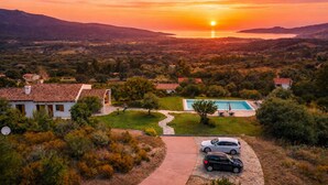 Un quartier résidentiel doté d’une piscine, de voitures garées et offrant une vue dégagée sur le coucher de soleil derrière les collines.