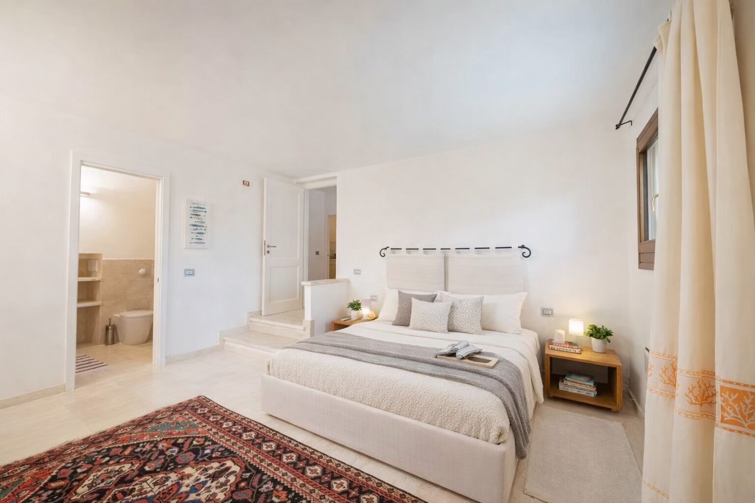 Ein modernes Schlafzimmer mit einem großen Bett, Nachttischen, einem Beistelltisch, einem gemusterten Teppich und einem durchgehenden Türspalt einsehbaren Badezimmer.