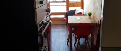 Una cocina compacta con zona de comedor, suelo de madera y vistas a través de un ventanal.