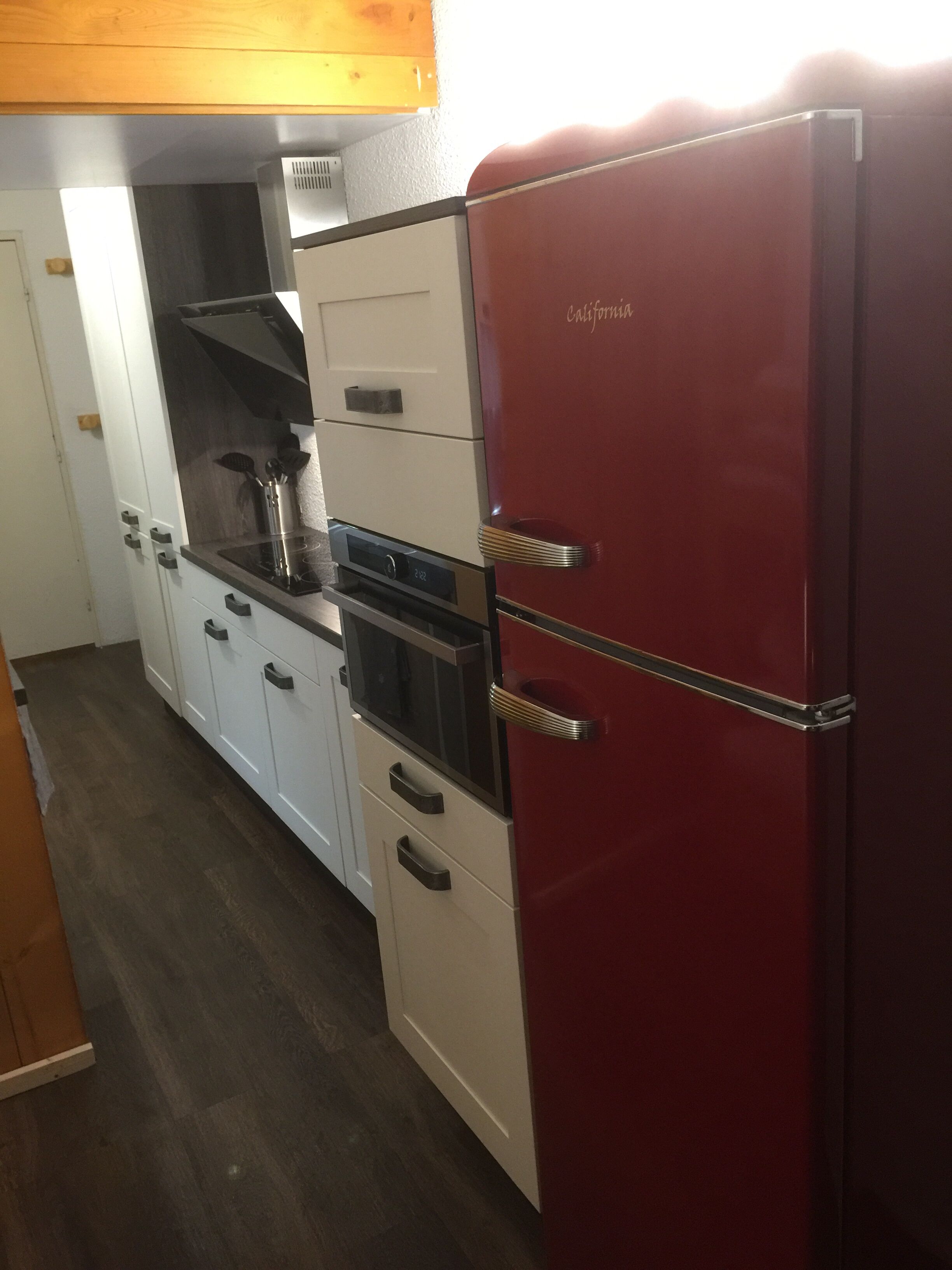 Een kleine keuken met witte kasten, een rode koelkast en een ingebouwde oven.