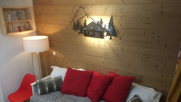 Ein gemütliches Zimmer mit einer Holzwand, einem weißen Sofa mit roten und grauen Kissen, einem roten Sessel und einer Lampe.