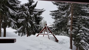 Schneebedeckte Landschaft mit einer hölzernen Schaukel im Vordergrund und immergrünen Bäumen im Hintergrund.
