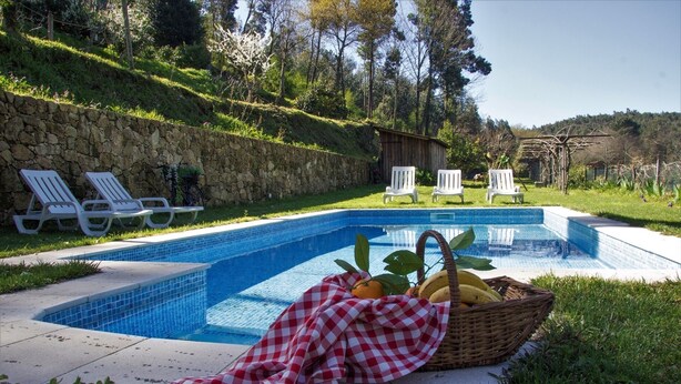 Una piscina con una parete in pietra, poltrone da relax bianche e un cesto di frutta.