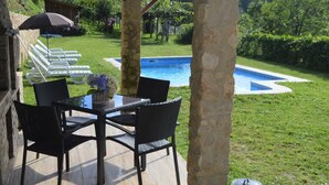 Patio esterno con tavolo e sedie, piscina e area verde con sdraio.