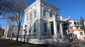 Un edificio grande y blanco con columnas y un balcón, rodeado de una valla y árboles.