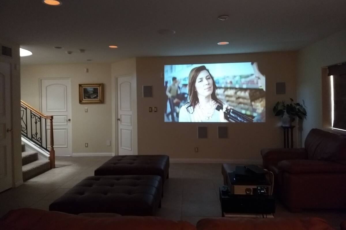 A living room with a large screen, ottomans, a sofa, and a staircase.