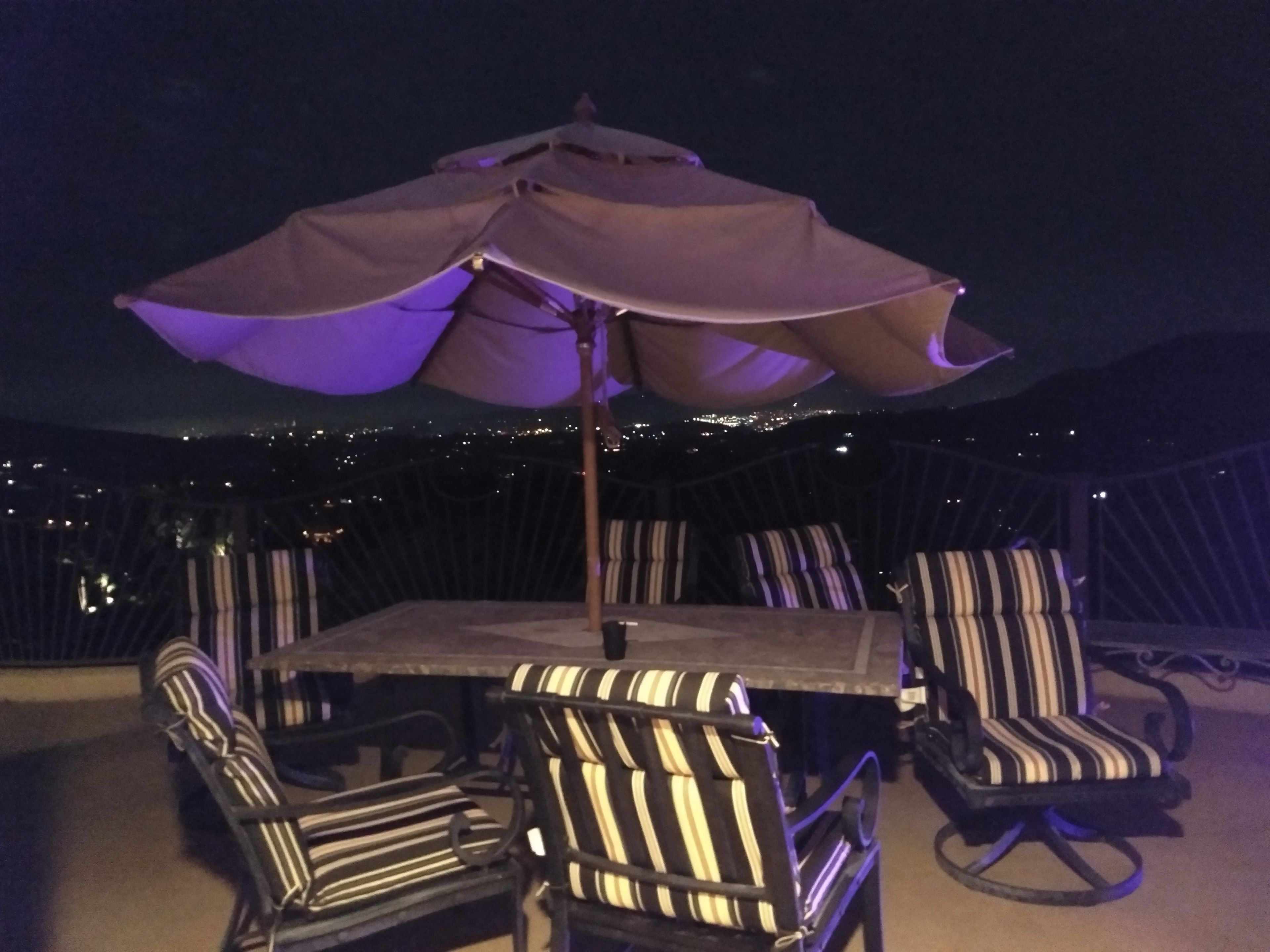 Un patio con una mesa y cuatro sillas a rayas, una sombrilla y una baranda con luces.