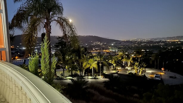 A nighttime view from a balcony overlooking a cityscape with illuminated buildings and palm trees. - Sunshine Mountain Bed and Breakfast (San Marcos)