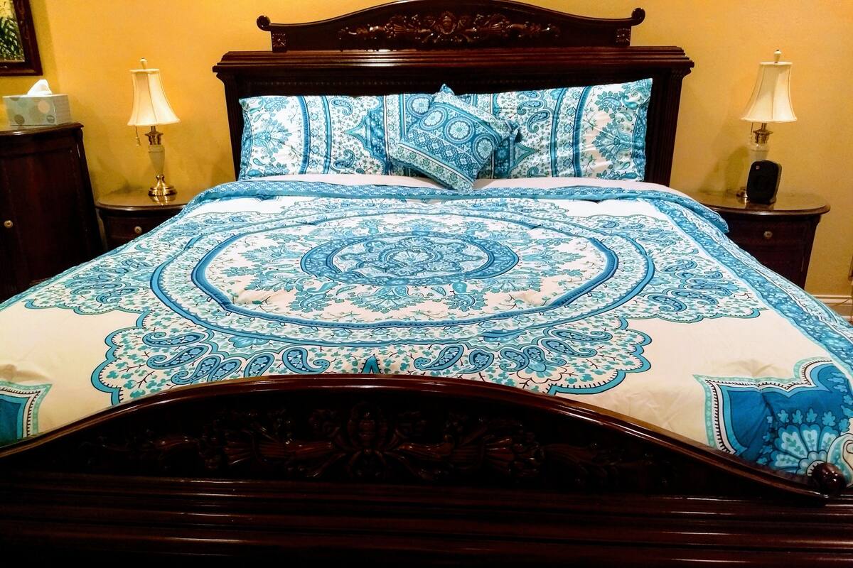 A bed with a blue and white patterned bedspread, wooden headboard, two bedside tables with lamps, and a wooden nightstand.