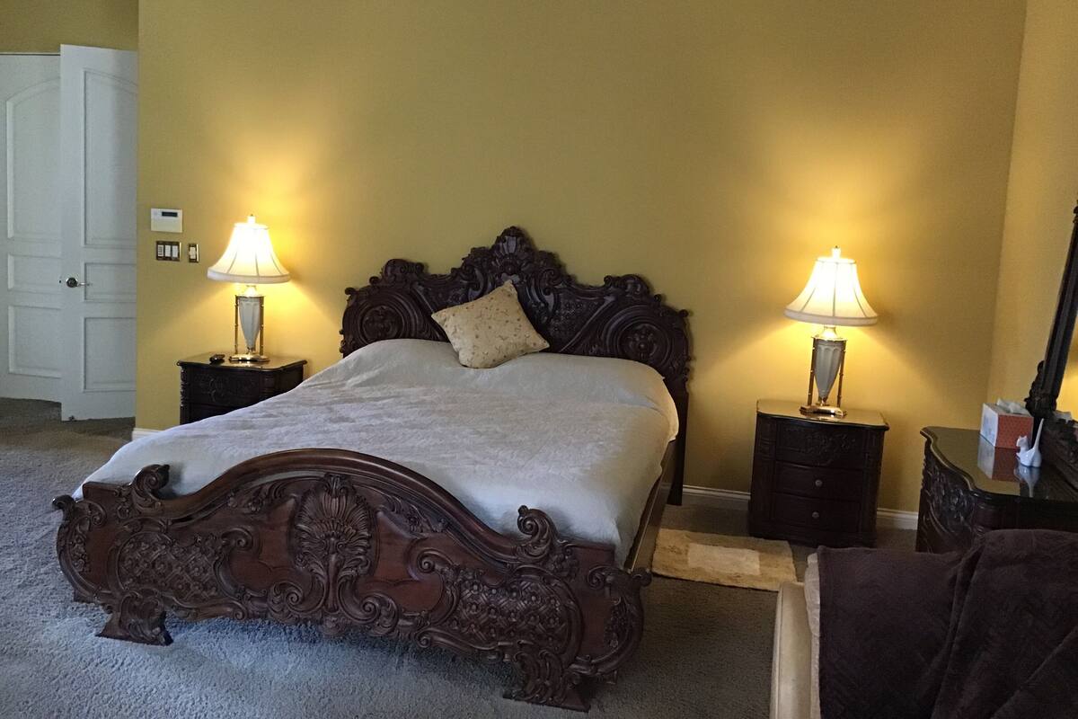 A bedroom with a large bed, two bedside tables with lamps, a wooden headboard, and a door.