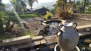 A garden with a stone fountain, a small pond, and a view of a distant town. - Sunshine Mountain Bed and Breakfast (San Marcos)