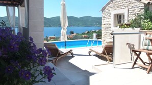 Un espace aménagé au bord de la piscine, avec un bâtiment en pierre, des chaises longues et une vue sur la mer.