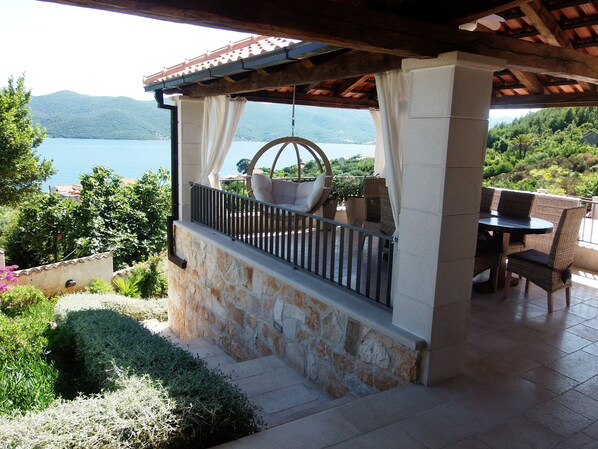 A balcony with a stone wall, a hanging chair, and a table with chairs.