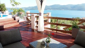 Une terrasse en bois avec des meubles en osier, une table en verre et des plantes en pot.