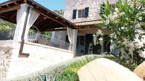 Un immeuble de deux étages avec une façade en pierre, des volets verts et un balcon doté d’une balustrade blanche.