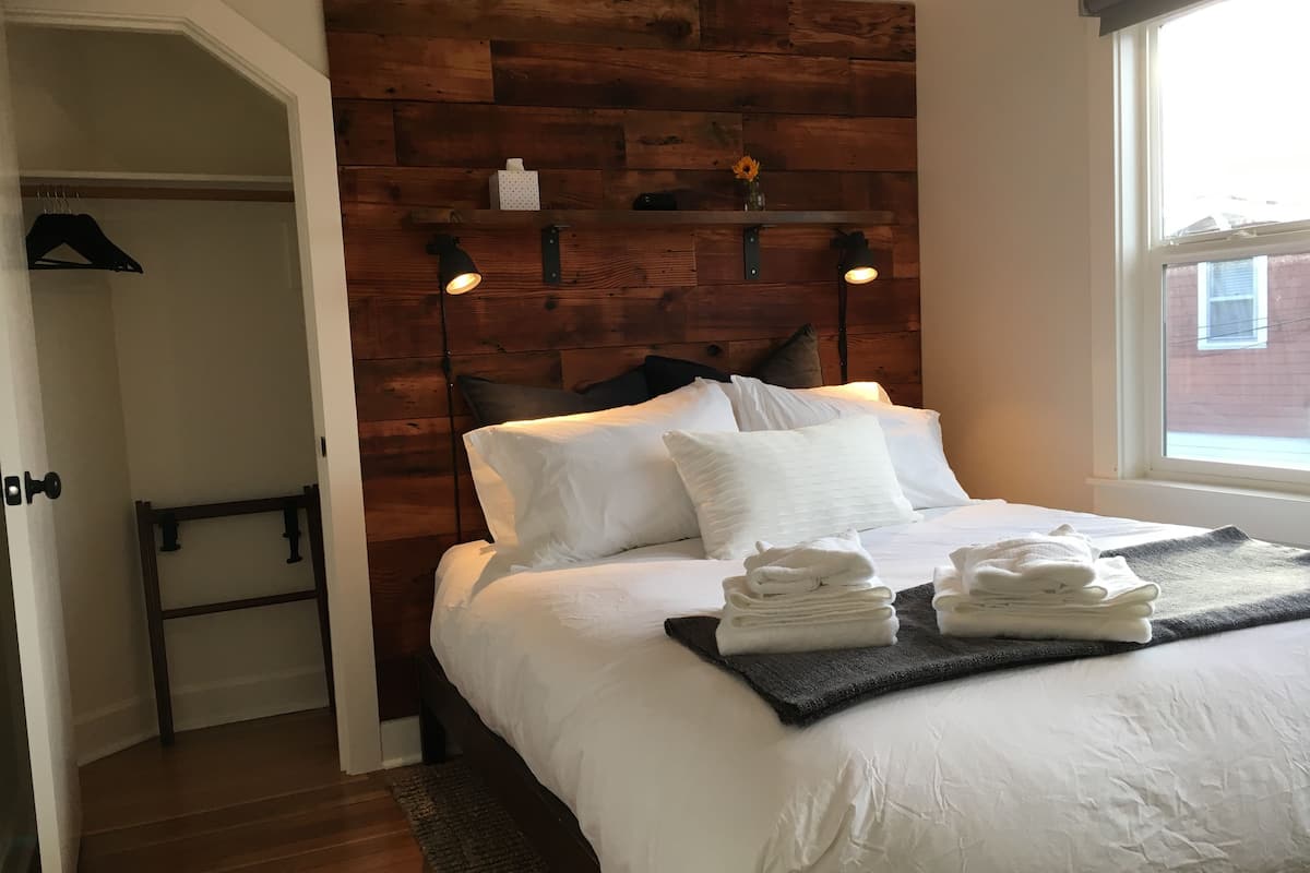 Un lit bien fait, avec du linge de lit et des serviettes blanches, une tête de lit en bois et deux lampes de lecture fixées au mur.
