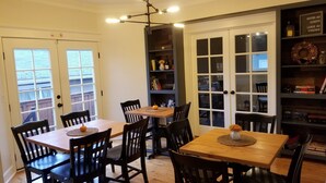 A dining area with two wooden tables and chairs, a bookshelf, and a door with a frosted glass panel. - The Alberta Petite Hotel (Portland)