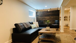 A modern living room with a black leather sofa, a wooden coffee table, and a small potted plant. - The Alberta Petite Hotel (Portland)