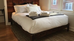 A neatly made bed with white linens, a dark wooden headboard, and a window with a view of a brick building. - The Alberta Petite Hotel (Portland)