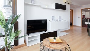 Een moderne woonkamer met een flatscreen televisie, witte kasten, een eettafel met stoelen en een potplant.