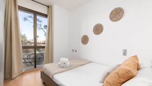 Een slaapkamer met een groot raam, een bed met witte lakens, een opgerolde handdoek en drie decoratieve items aan de muur.