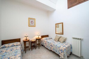 Un dormitorio con dos camas individuales, una mesita, una silla, una lámpara de noche, un espejo y un radiador.