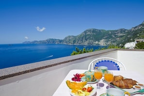 Une table dressée avec des aliments pour le petit-déjeuner, une vue sur la mer et un paysage montagneux en arrière-plan.