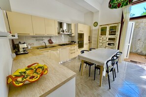 A kitchen with beige cabinets, a white countertop, a dining table with chairs, and a decorative fruit bowl.