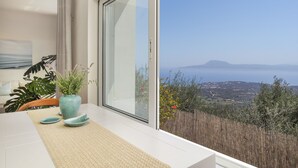 Un espace repas moderne avec une grande fenêtre, une table agrémentée d’un set de table, un vase avec des plantes et une vue sur le paysage.