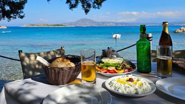 Une table avec de la nourriture et des boissons, une bouteille verte, et une vue sur la mer et les montagnes.