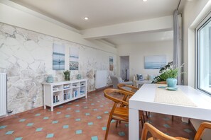Een moderne eetruimte met een witte tafel, houten stoelen, een witte console met boeken en een stenen muur met kunstwerken.