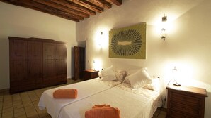 Un dormitorio con un amplio armario de madera, una cama con ropa blanca y una lámpara fijada a la pared.