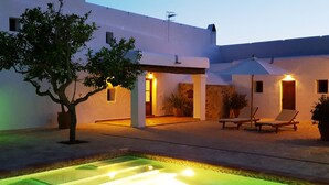 Un edificio moderno y blanco con piscina, sillones de descanso y plantas en macetas.
