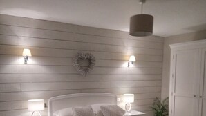 Un dormitorio con cama, dos mesitas de noche con lámparas, una lámpara de techo, una planta y un armario.