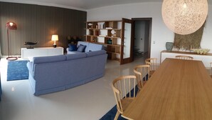 Una sala de estar moderna con un sofá, una mesa de comedor de madera y sillas. Hay una estantería y un espejo grande en la pared.