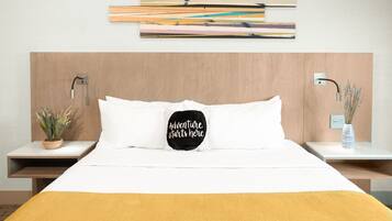Een verzorgde hotelkamer met een bed, nachtkastje met een plant, een kunstwerk aan de muur en een decoratief kussen.