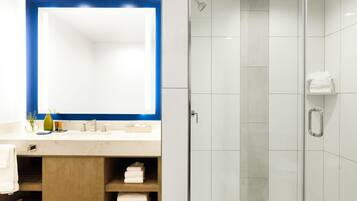 A modern bathroom with a glass shower enclosure, a large mirror, and a vanity with a sink and towel storage.