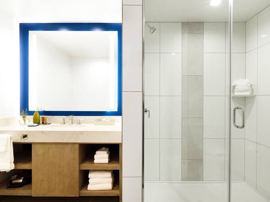 A modern bathroom with a glass shower enclosure, a large mirror, and a vanity with a sink and towel storage.
